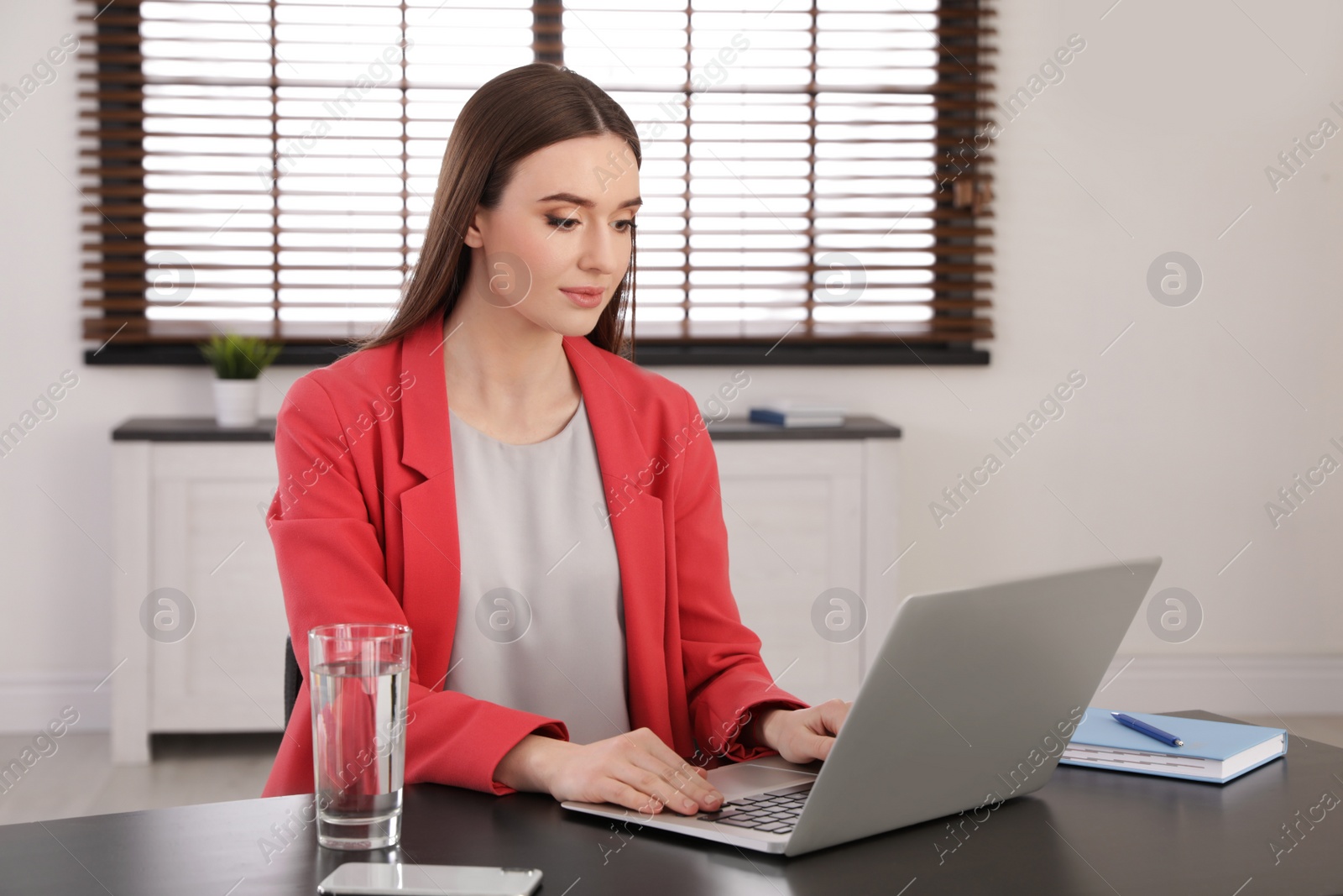 Photo of Young businesswoman using laptop at table in office