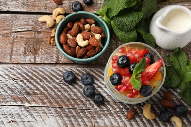 Photo of Delicious fruit salad, fresh berries, mint and nuts on wooden table, flat lay. Space for text