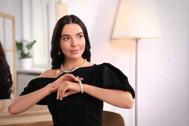 Photo of Young woman trying on elegant pearl bracelet indoors, space for text