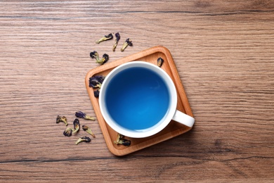 Photo of Organic blue Anchan in cup on wooden table, flat lay. Herbal tea