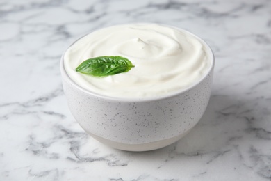 Bowl of fresh sour cream with basil on white marble table