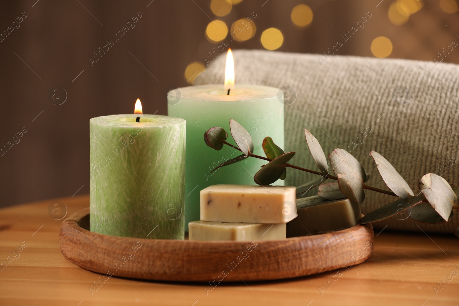 Photo of Spa composition. Burning candles, soap, towel and eucalyptus branch on wooden table