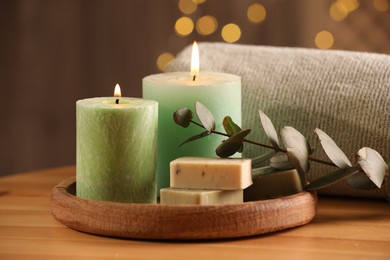 Photo of Spa composition. Burning candles, soap, towel and eucalyptus branch on wooden table