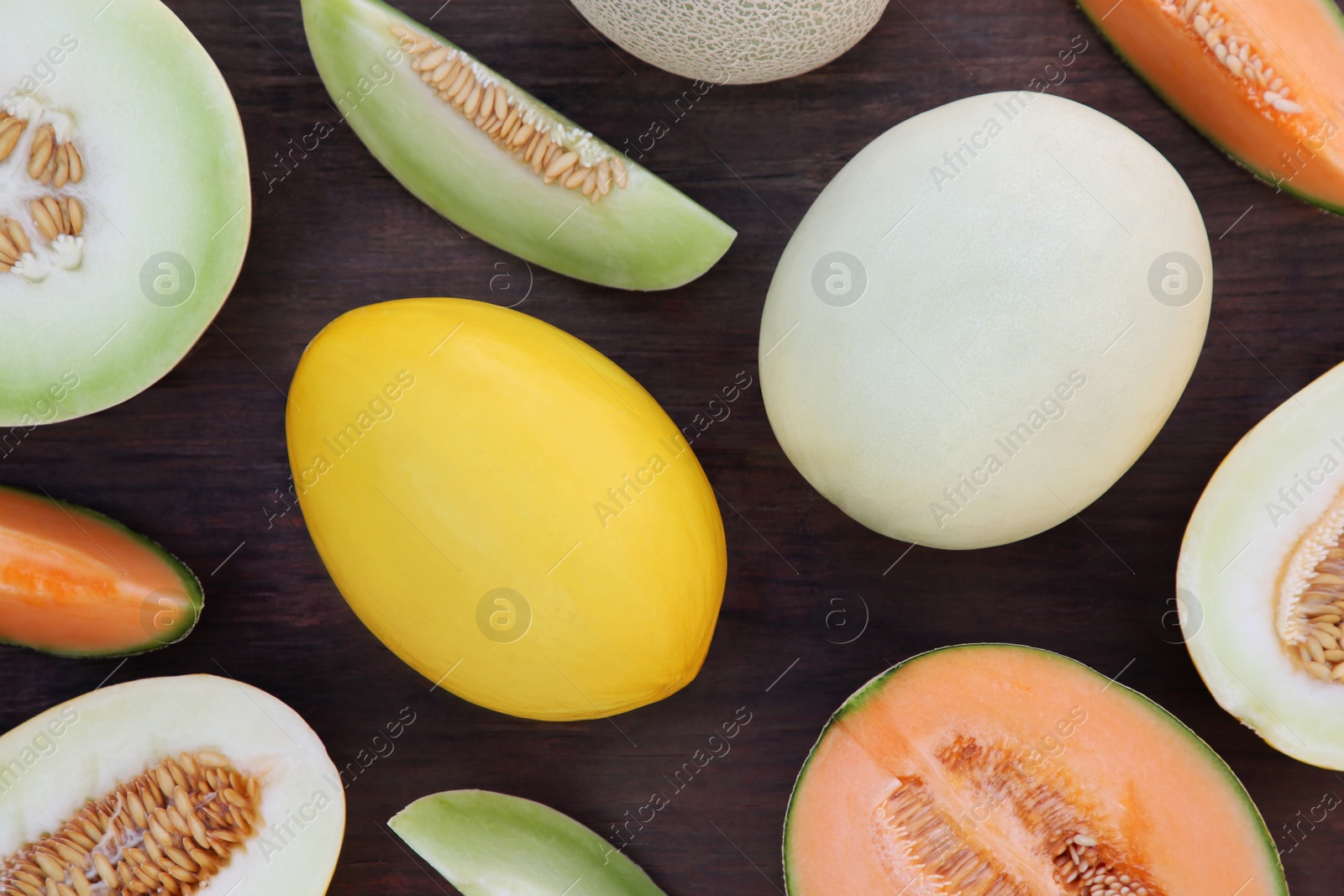 Photo of Different types of tasty ripe melons on wooden table, flat lay