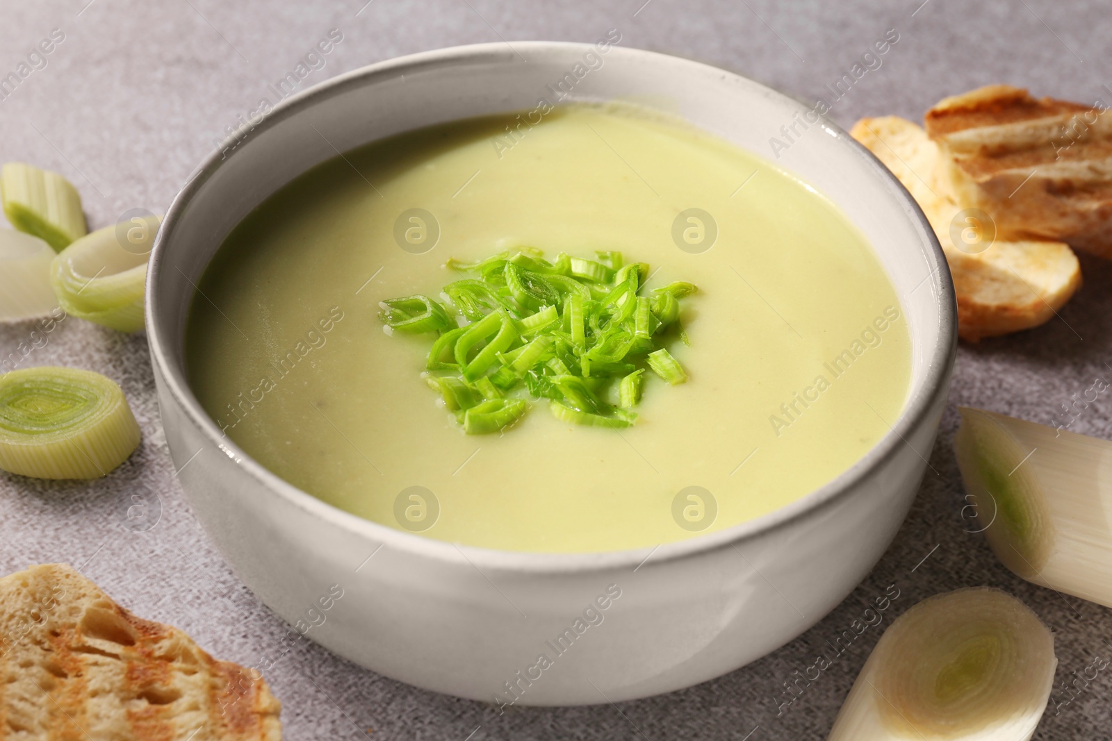 Photo of Bowl of delicious soup, cut leek and croutons on grey table, closeup