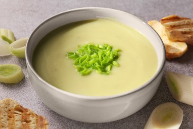 Photo of Bowl of delicious soup, cut leek and croutons on grey table, closeup
