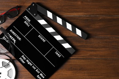 Photo of Clapperboard, film reel and 3D glasses on wooden table, flat lay. Space for text