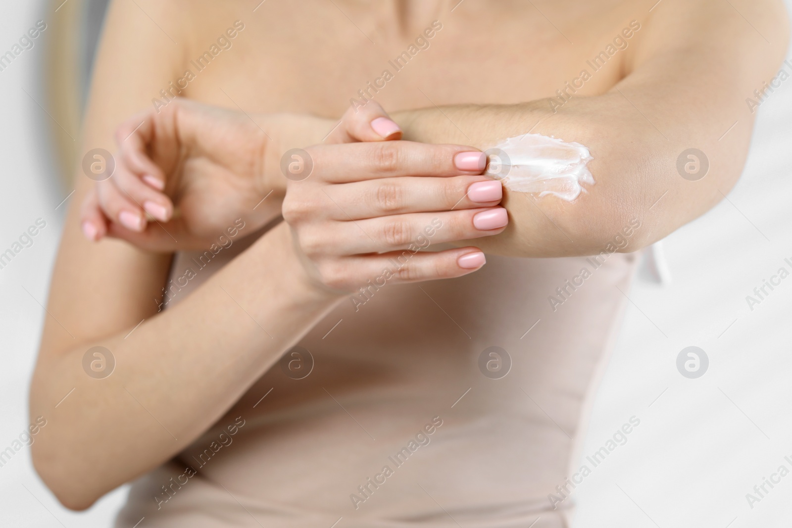 Photo of Woman applying body cream onto elbow on blurred background, closeup