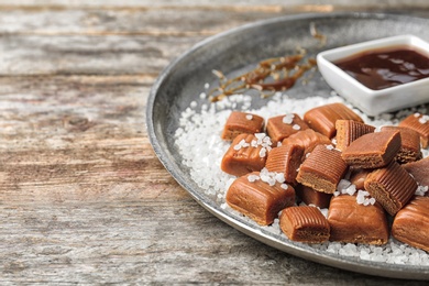 Plate with delicious caramel candies, sauce and salt on table