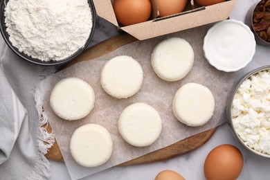 Photo of Uncooked cottage cheese pancakes and different ingredients on white marble table, flat lay