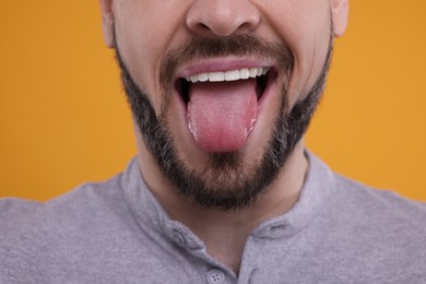 Photo of Happy man showing his tongue on orange background, closeup