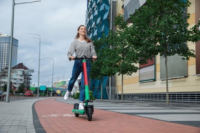 Photo of Happy woman riding modern electric kick scooter on city street, space for text
