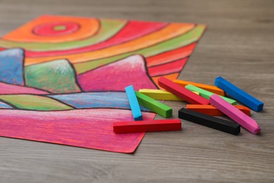 Photo of Beautiful drawing and pastels on wooden table, closeup view