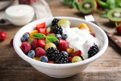 Photo of Fresh tasty fruit salad with yogurt on wooden table, closeup