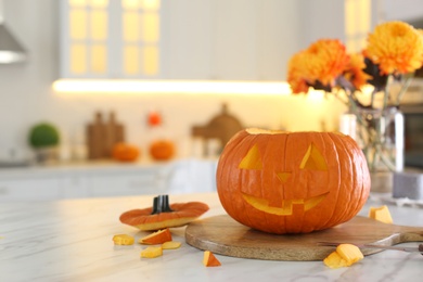 Photo of Pumpkin jack o'lantern on white marble table in kitchen, space for text. Halloween celebration