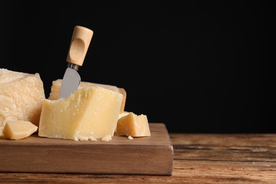 Parmesan cheese with knife on wooden table, closeup. Space for text