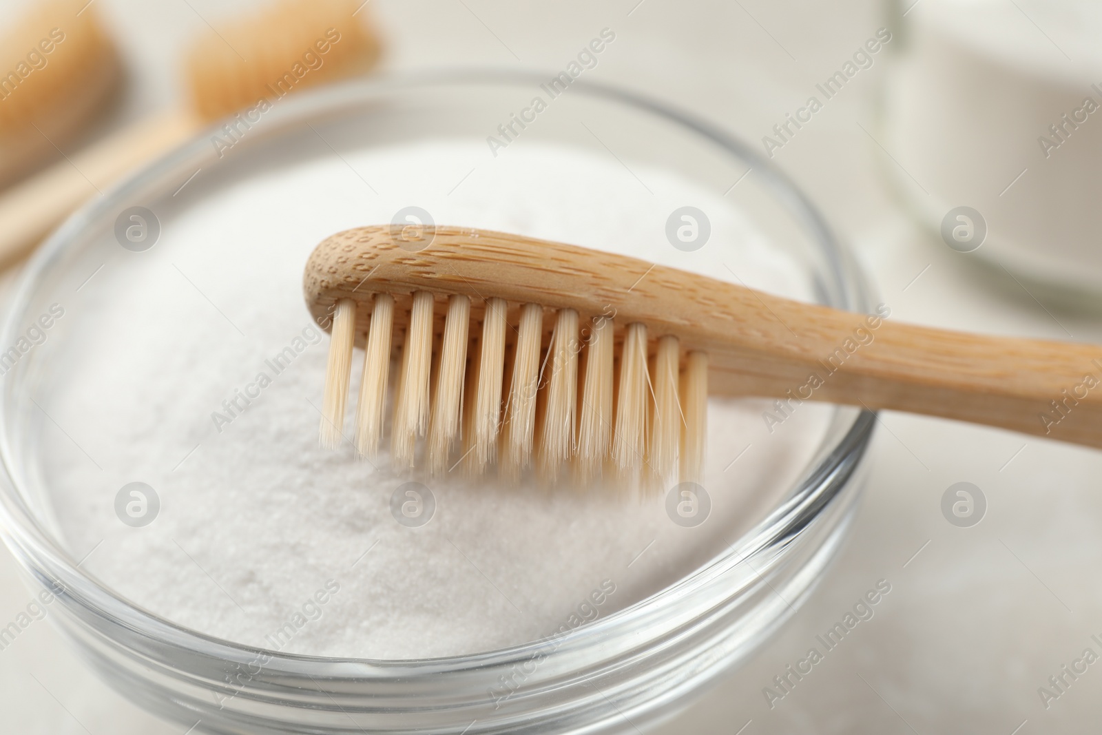 Photo of Bamboo toothbrush and glass bowl of baking soda on light table, closeup