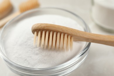 Bamboo toothbrush and glass bowl of baking soda on light table, closeup