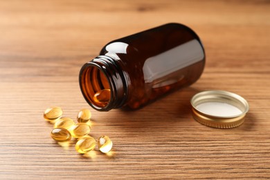 Overturned bottle with dietary supplement capsules on wooden table