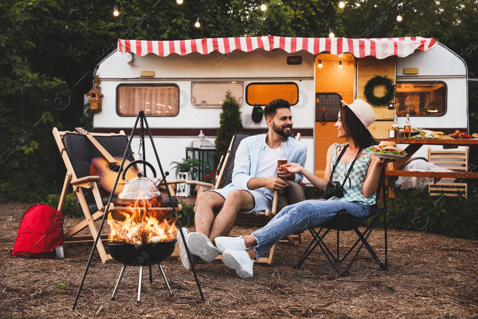 Image of Happy couple resting near trailer. Camping season