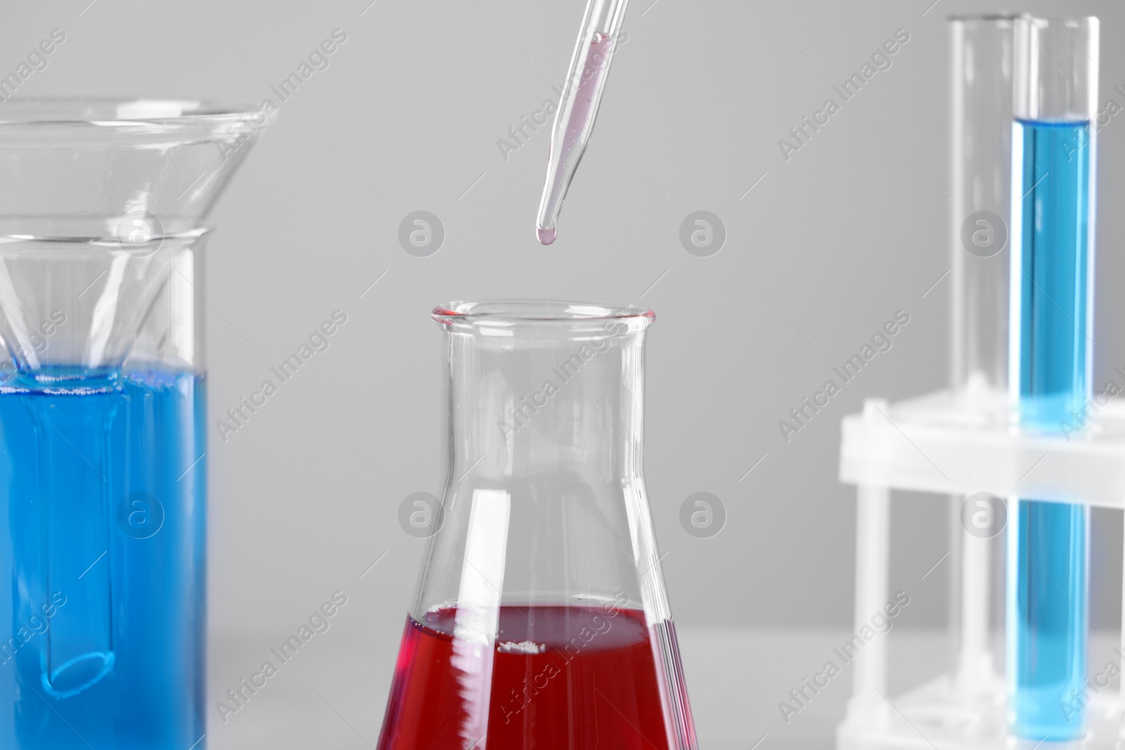 Photo of Dripping liquid from pipette into flask on grey background, closeup