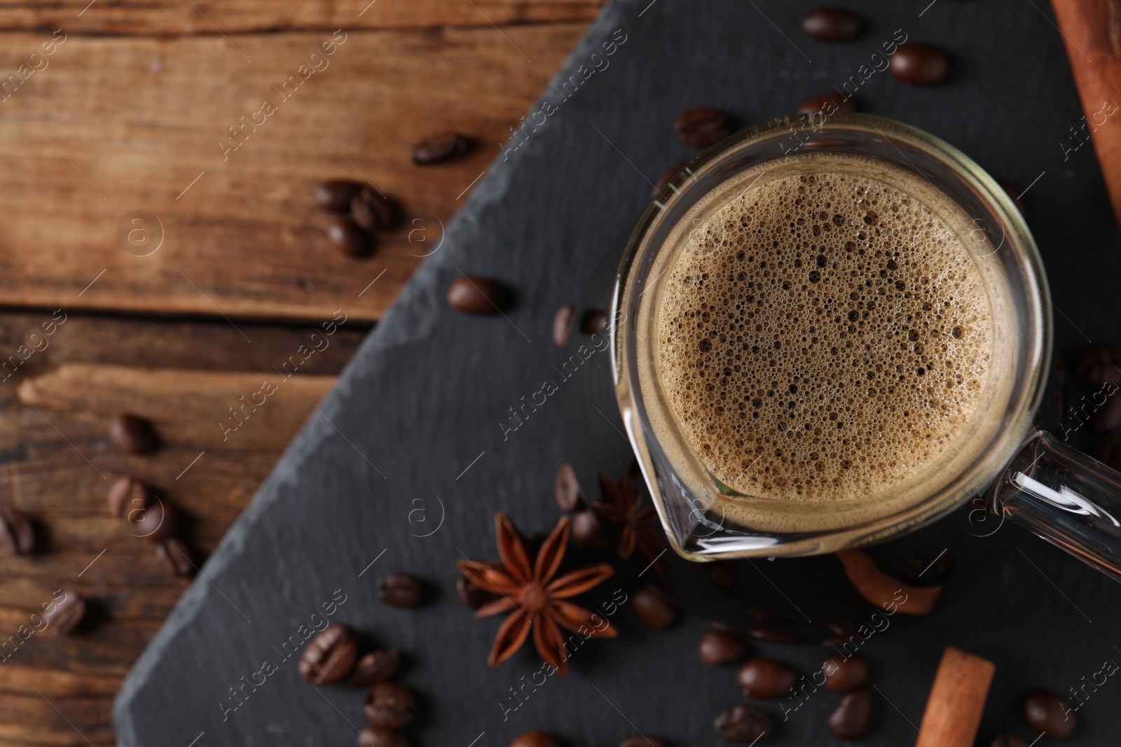 Photo of Turkish coffee in glass cezve, beans and spices on wooden table, flat lay. Space for text