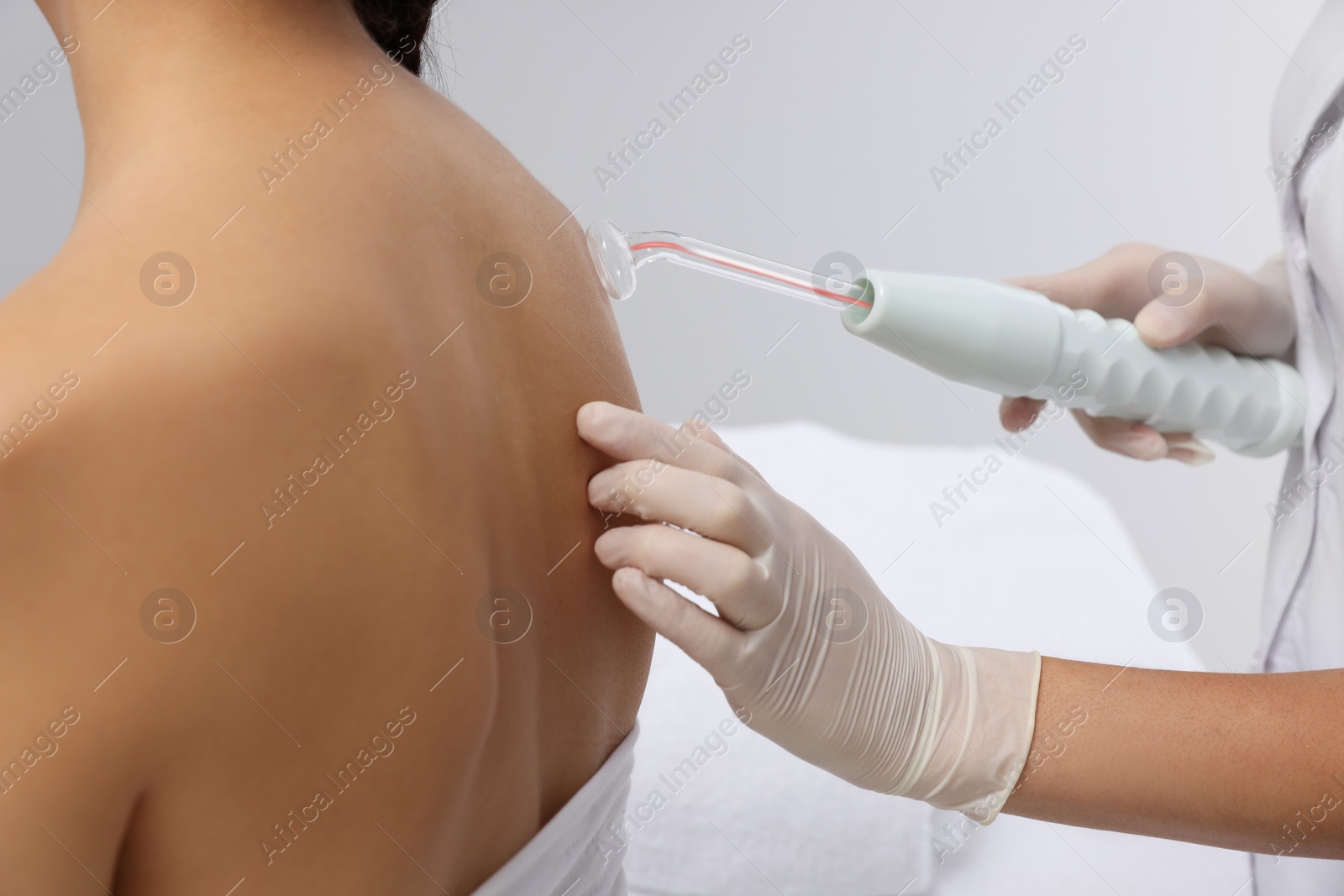 Photo of Woman undergoing physiotherapy procedure with darsonval in salon, back view