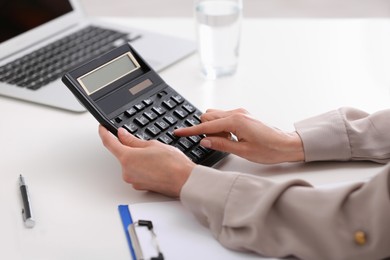 Photo of Woman using calculator at table indoors, closeup