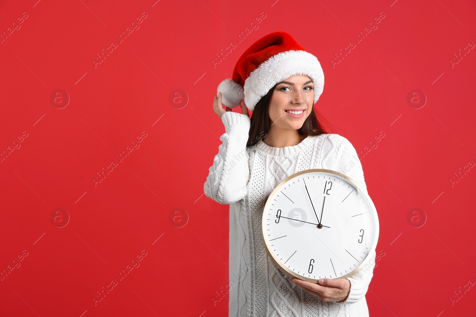 Photo of Young beautiful woman in Santa hat holding big clock on color background. Christmas celebration