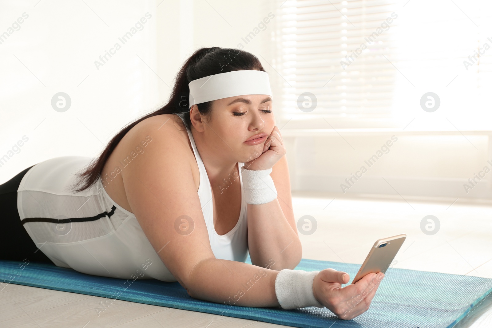 Photo of Lazy overweight woman using mobile phone instead of training at gym