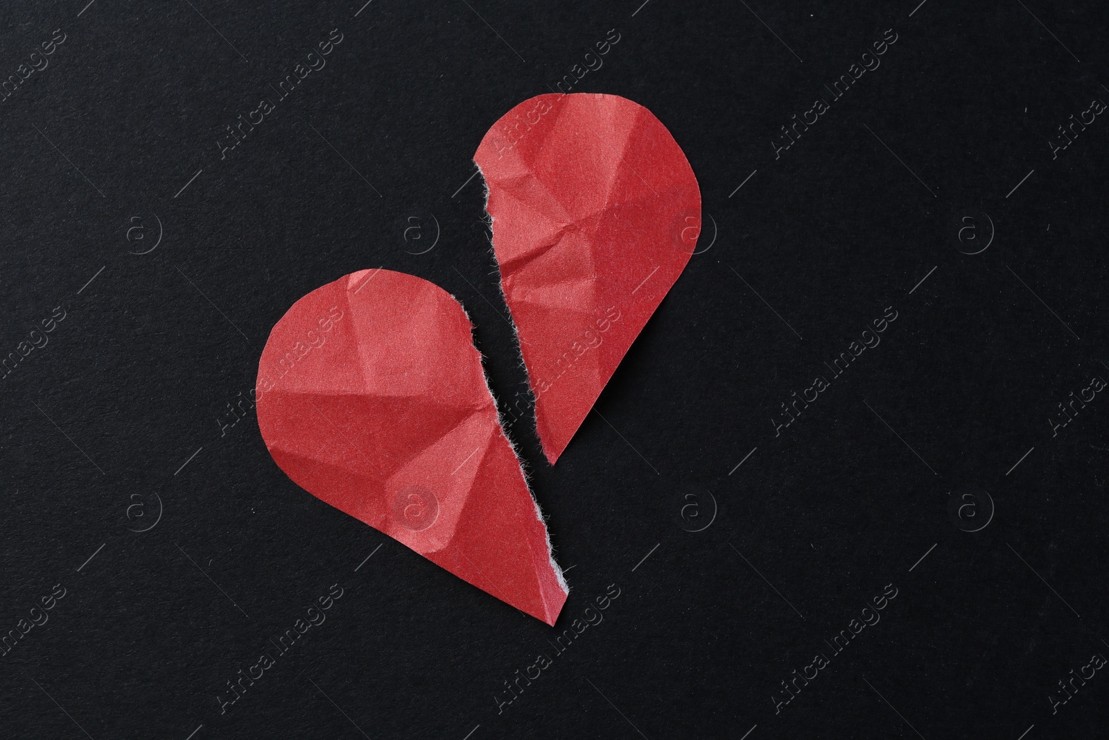 Photo of Halves of torn paper heart on black background, top view. Breakup concept
