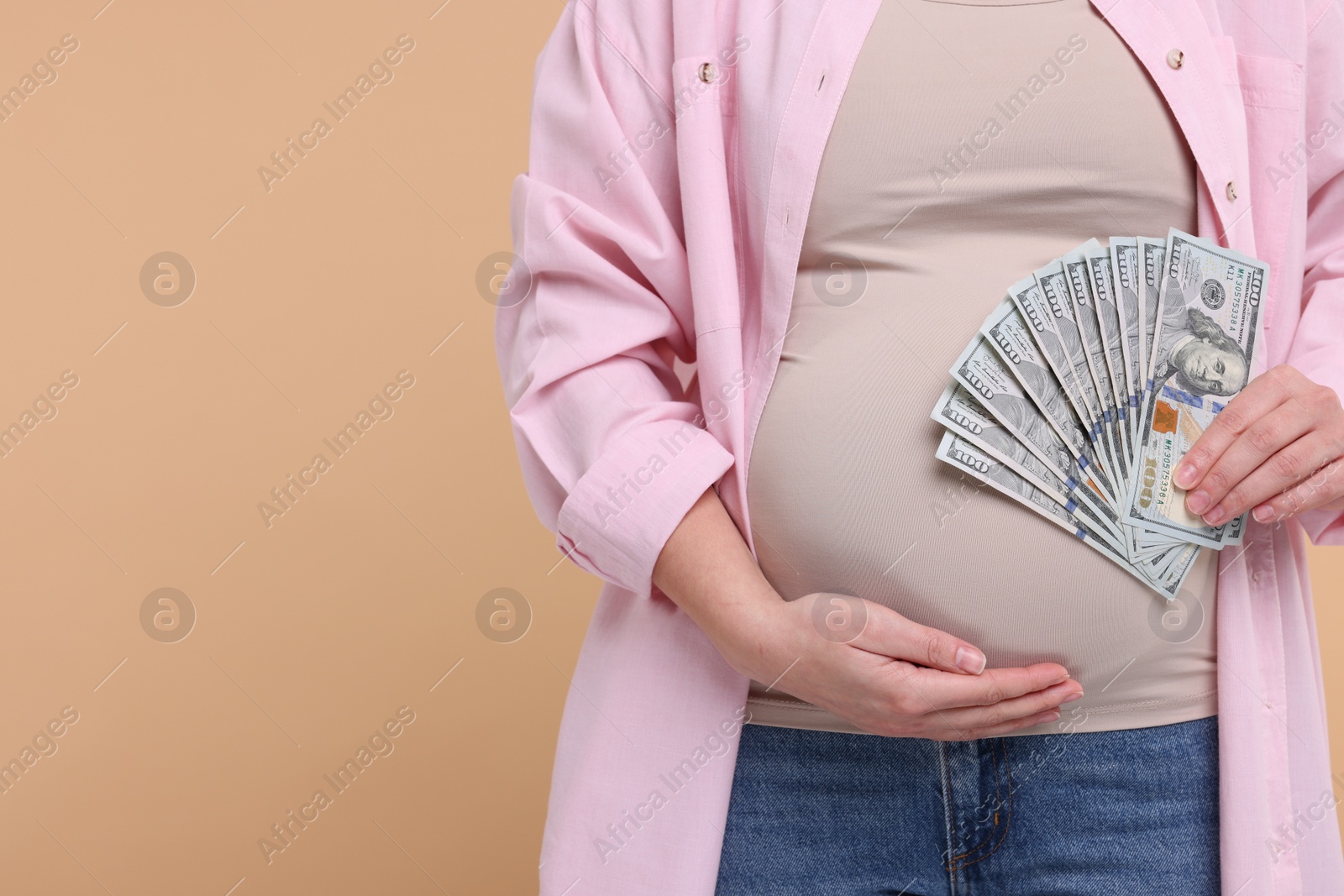 Photo of Surrogate mother. Pregnant woman with dollar banknotes on beige background, closeup. Space for text