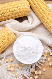 Photo of Bowl with corn starch, ripe cobs and kernels on wooden table, flat lay