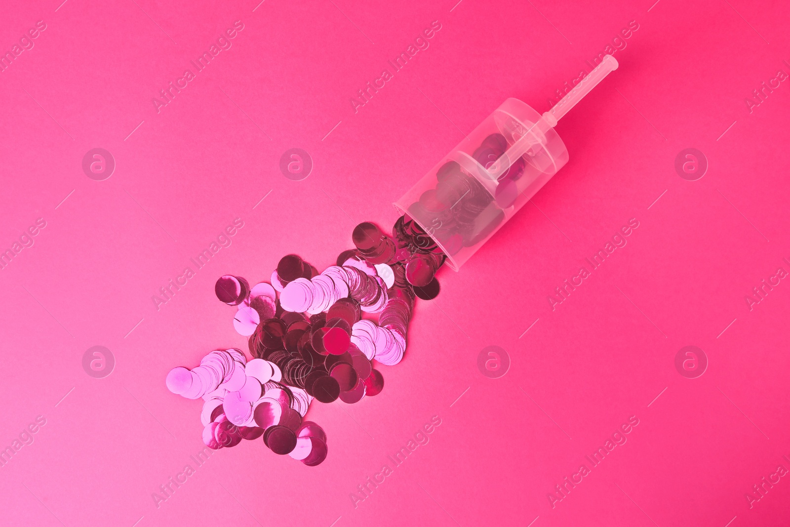 Photo of Shiny confetti bursting out of transparent party popper on pink background, flat lay