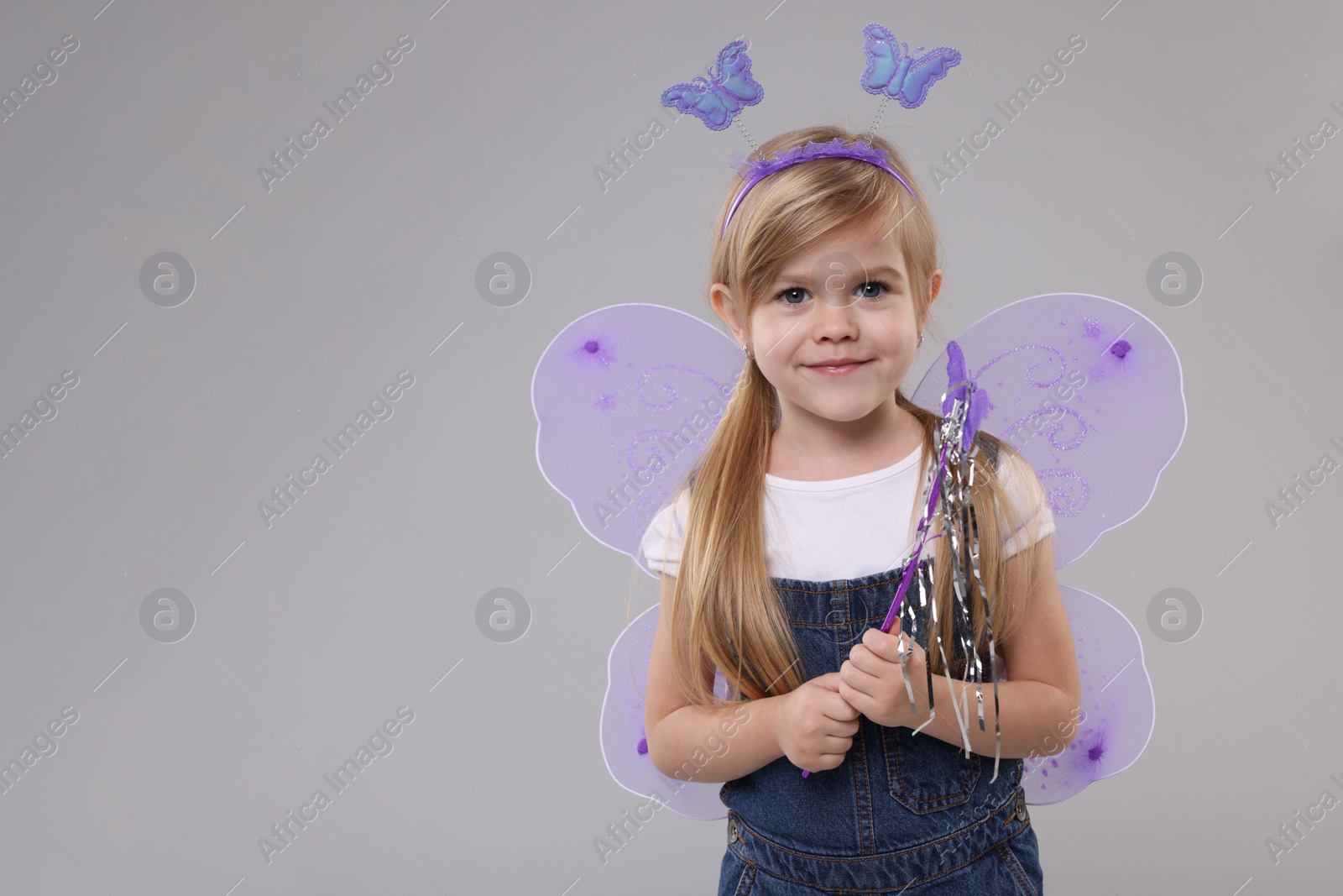 Photo of Cute little girl in fairy costume with violet wings and magic wand on light grey background, space for text