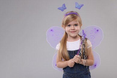Cute little girl in fairy costume with violet wings and magic wand on light grey background, space for text
