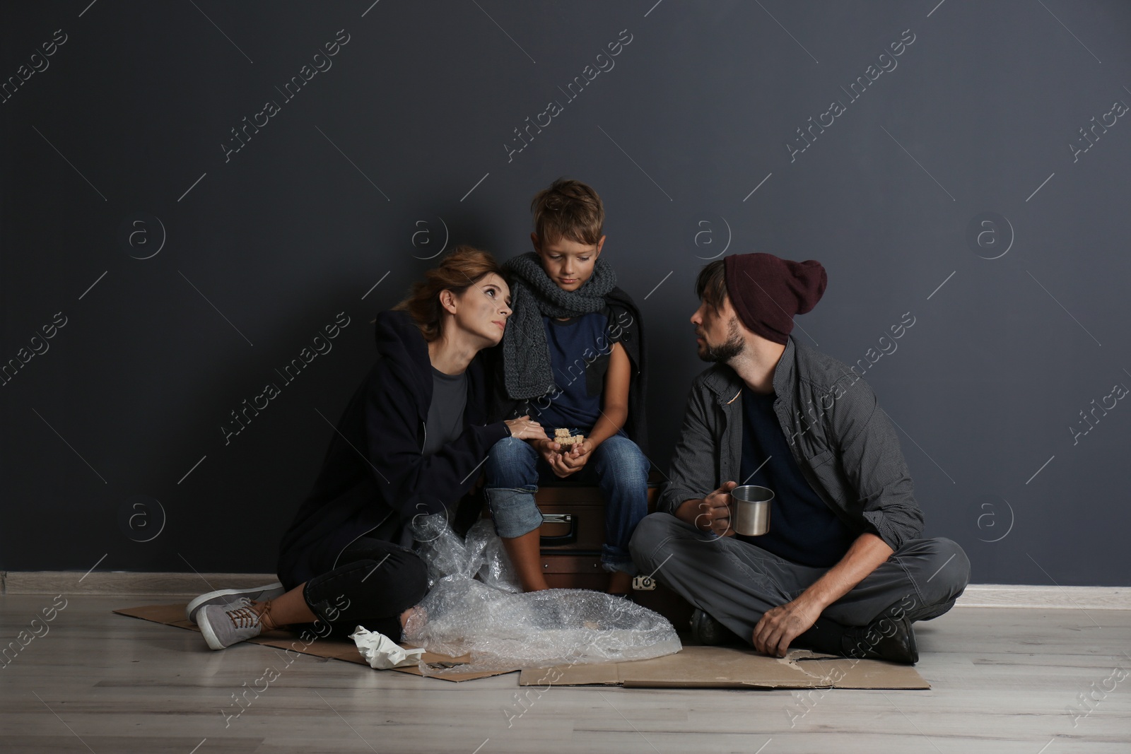 Photo of Poor homeless family sitting on floor near dark wall