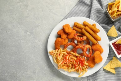 Different delicious fast food served with ketchup on light grey marble table, flat lay. Space for text