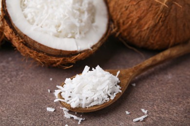 Photo of Coconut flakes and spoon on brown table, closeup