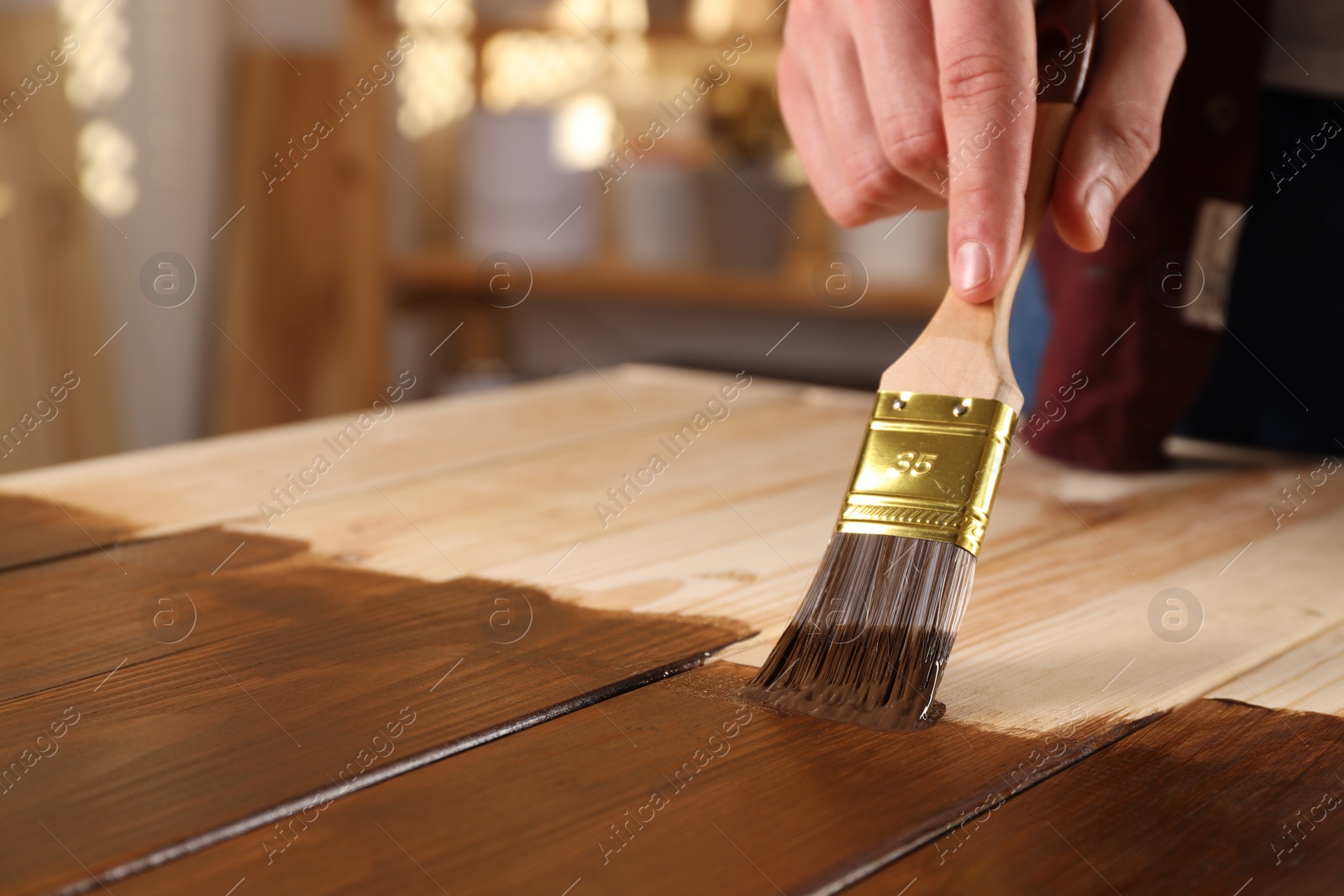Photo of Man with brush applying wood stain onto wooden surface indoors, closeup. Space for text