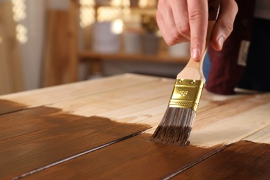 Photo of Man with brush applying wood stain onto wooden surface indoors, closeup. Space for text