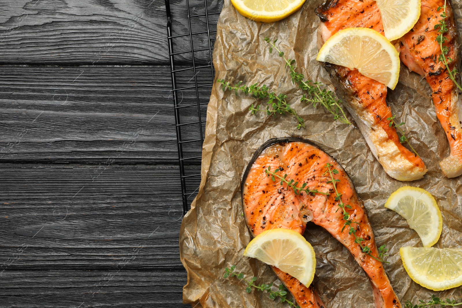 Photo of Tasty grilled salmon steaks and ingredients on black wooden table, top view. Space for text