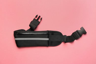 Photo of Stylish black waist bag on pink background, top view
