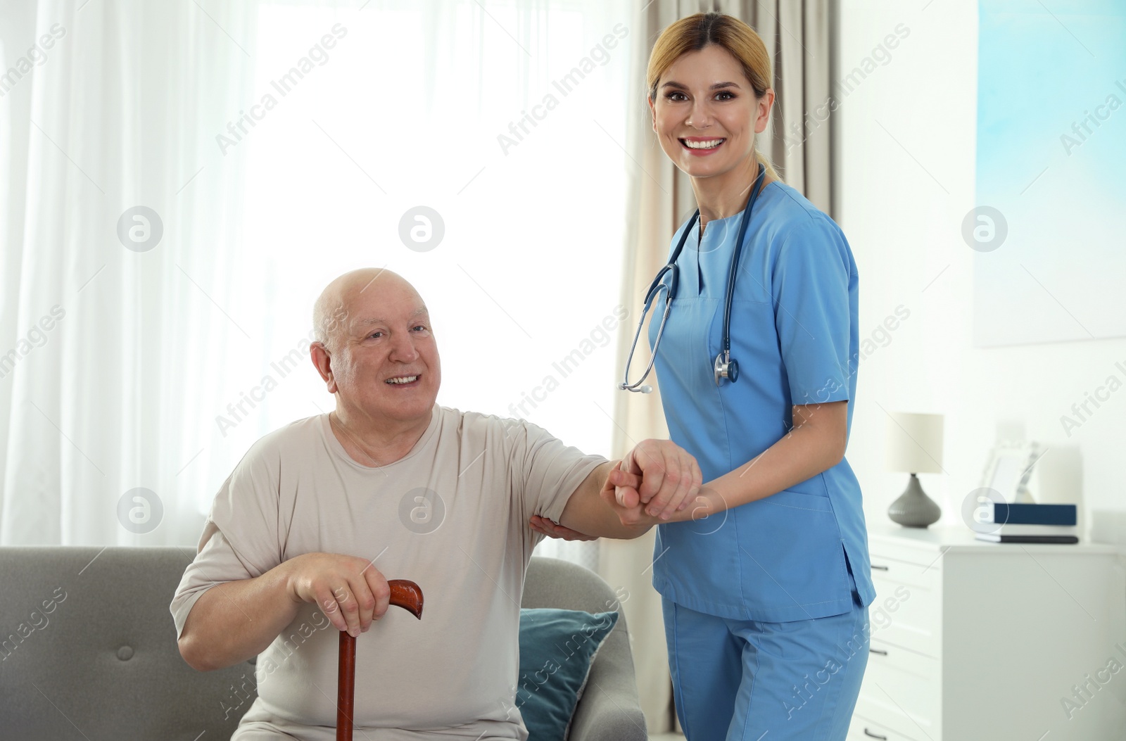 Photo of Nurse assisting elderly man with cane indoors