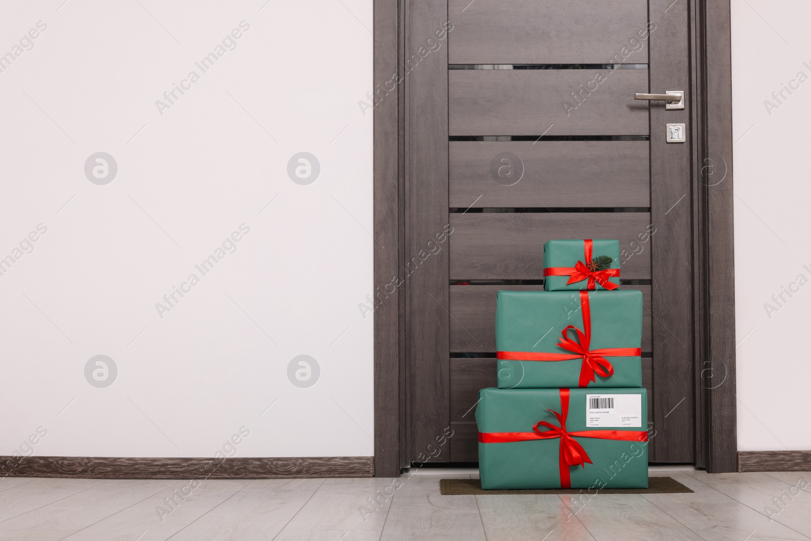 Photo of Christmas gift boxes on floor near door, space for text. Sending present by mail