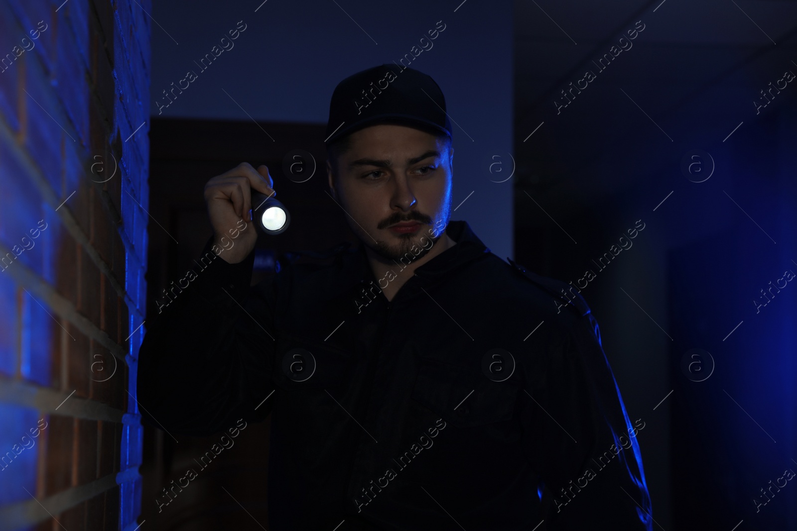 Photo of Male security guard with flashlight in dark corridor