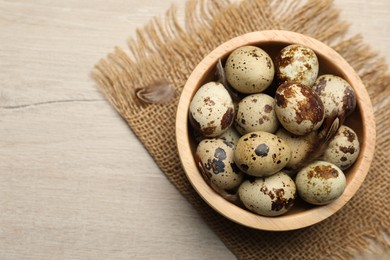 Photo of Speckled quail eggs on white wooden table, top view. Space for text