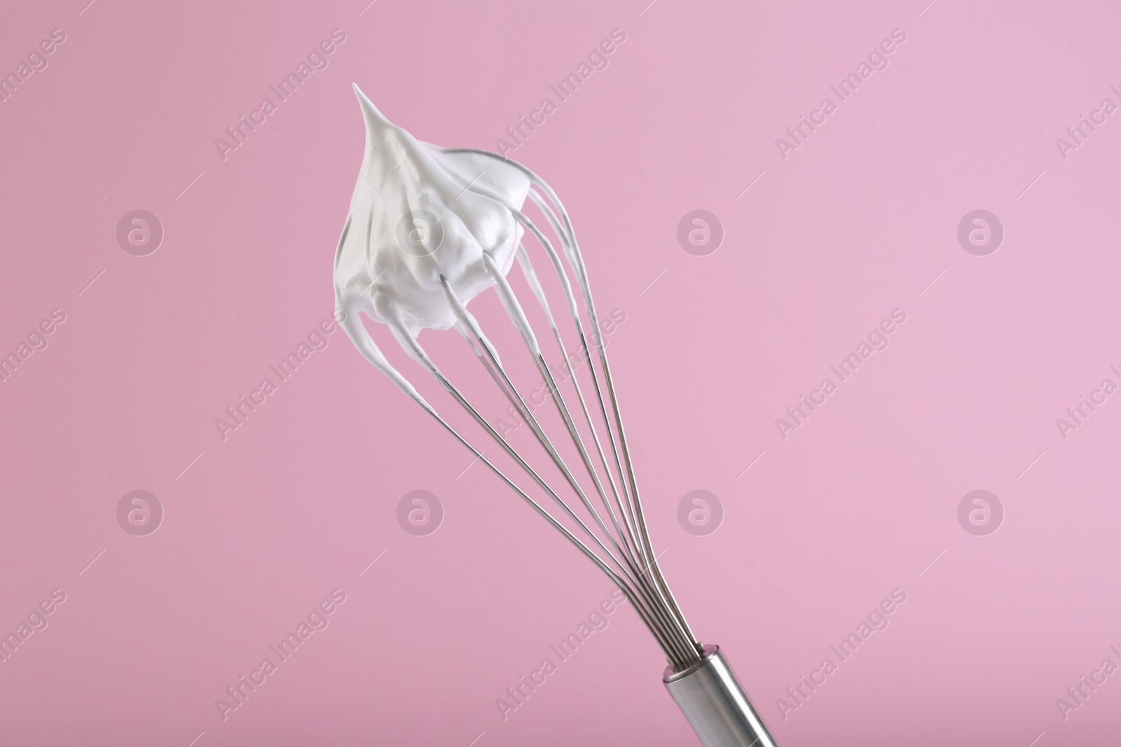 Photo of Whisk with whipped cream on pink background