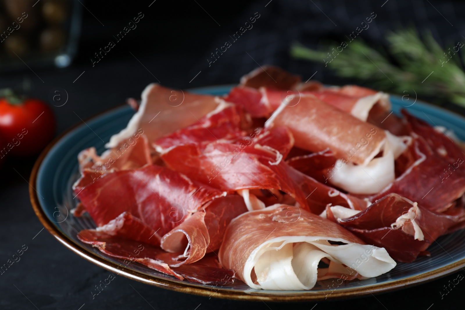 Photo of Tasty fresh prosciutto on black table, closeup