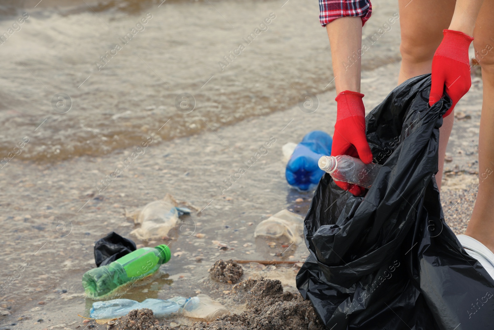 Photo of Woman in gloves with trash bag collecting garbage on beach, closeup